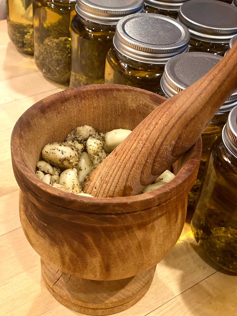 A wooden mortar and pestle with fresh garlic and herbs